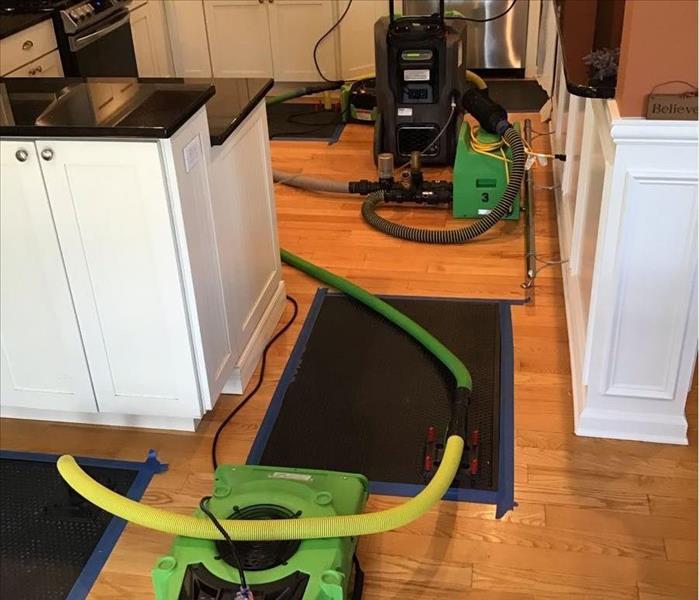 Air movement and dehumidification equipment in a kitchen with three drying mats taped down to a wet wood floor